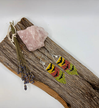 Long seed bead fringe earrings featuring bats on a yellow, carnelian, and yellow background with moonstone accents sitting on a rustic piece of wood.
