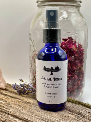 Facial toner bottle with label on a wooden surface with dried flowers and a jar in the background.