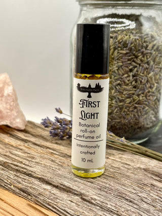 Roll-on perfume oil bottle labeled 'First Light' on a wooden surface with lavender and a crystal.