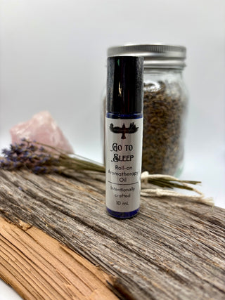 Roll-on aromatherapy oil bottle labeled 'Go To Sleep' on a wooden surface with lavender and a jar in the background.
