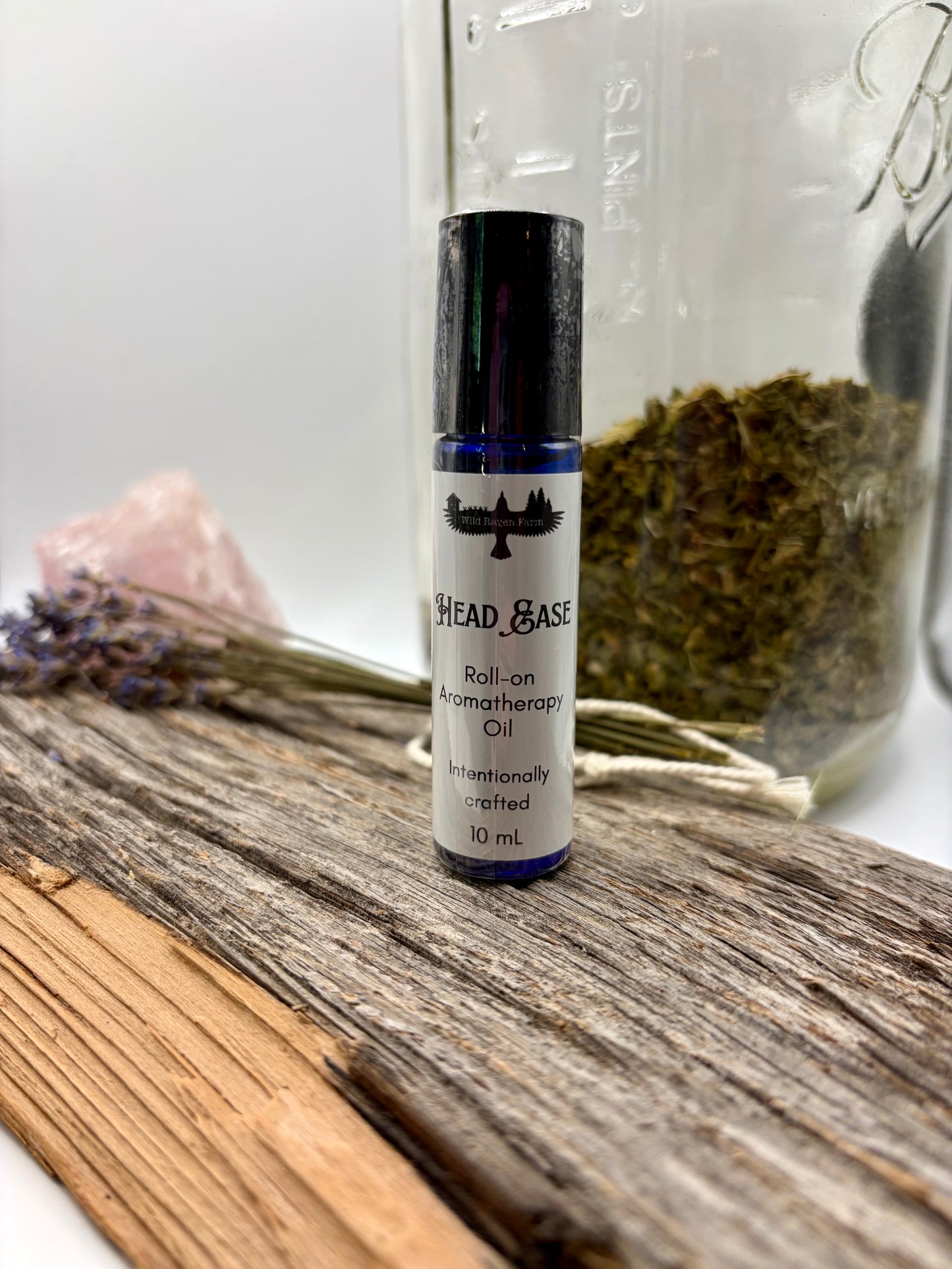 Roll-on aromatherapy oil bottle labeled 'Head & Base' on a wooden surface with herbs and a crystal in the background.