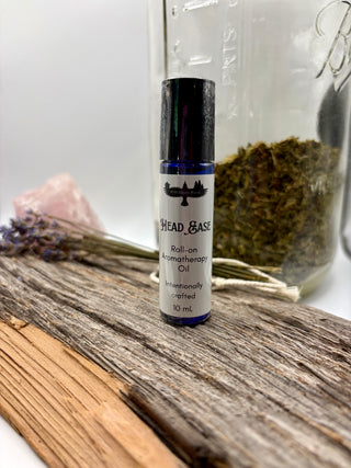 Roll-on aromatherapy oil bottle labeled 'Head & Base' on a wooden surface with herbs and a crystal in the background.