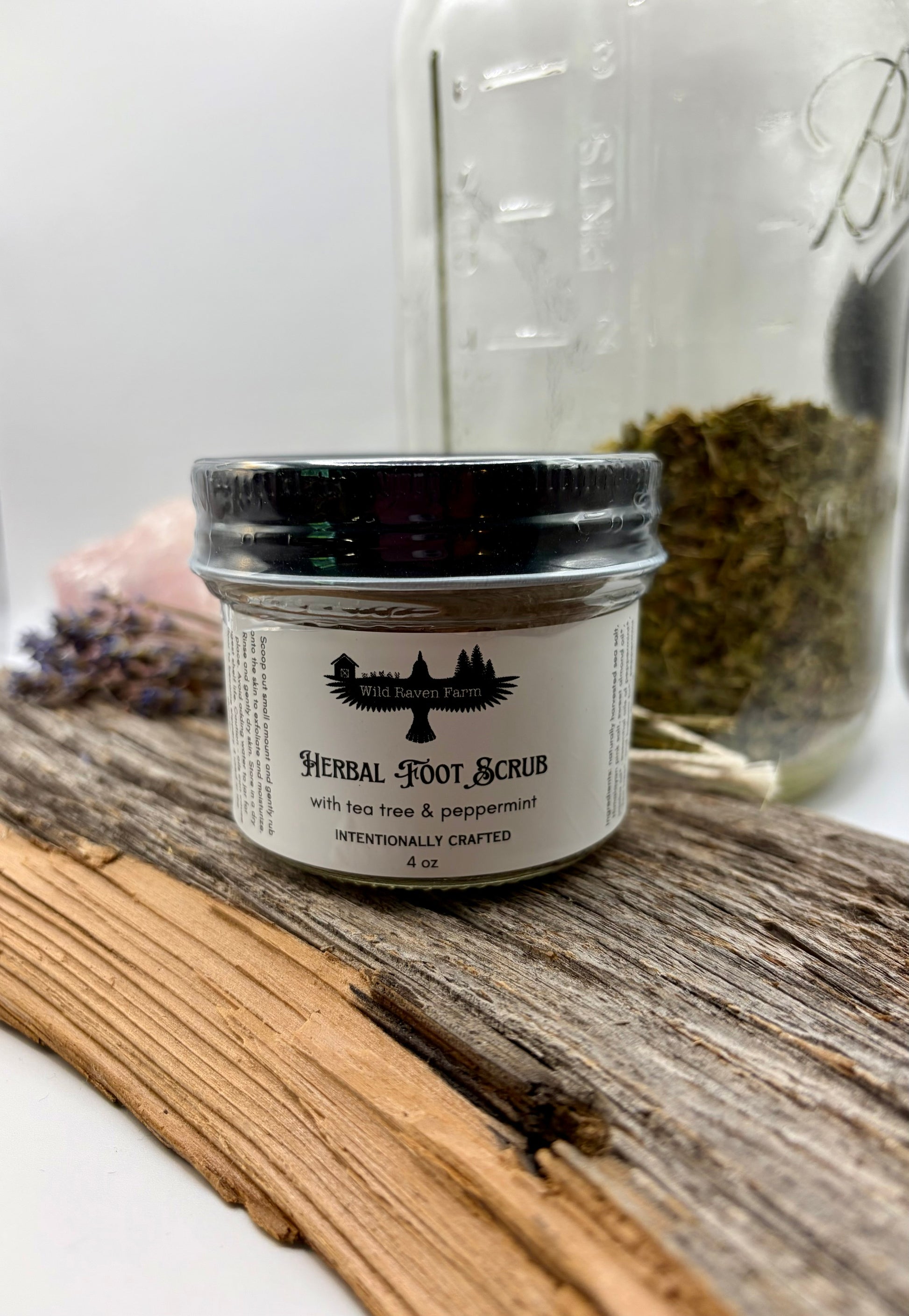 Jar of herbal foot scrub with a jar of herbs in the background on a wooden surface.