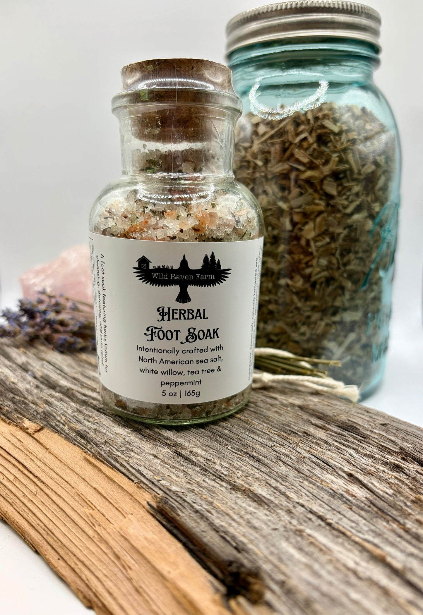 Herbal foot soak bottle with a jar of herbs on a wooden surface