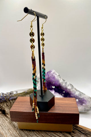 Pair of beaded earrings on a wooden stand with a crystal in the background