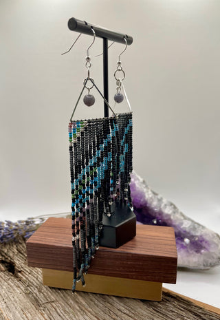 Beaded earrings on a wooden stand with crystals in the background