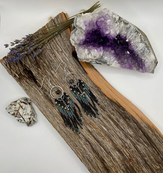Pair of beaded earrings on a wooden surface with an amethyst crystal and lavender flowers.