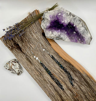 Beaded earrings on a wooden surface next to an amethyst crystal.