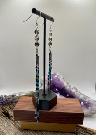 Pair of beaded earrings on a wooden stand with a crystal background