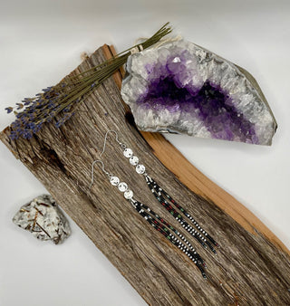 Pair of beaded earrings on a wooden surface with a crystal and dried lavender.