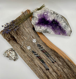 Pair of beaded earrings on a wooden surface with an amethyst crystal and lavender flowers.