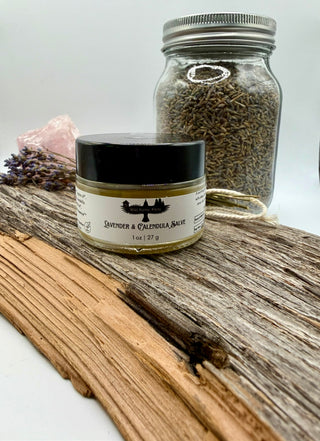 Small jar of lavender and calendula salve on a wooden surface with a larger jar of dried herbs in the background.