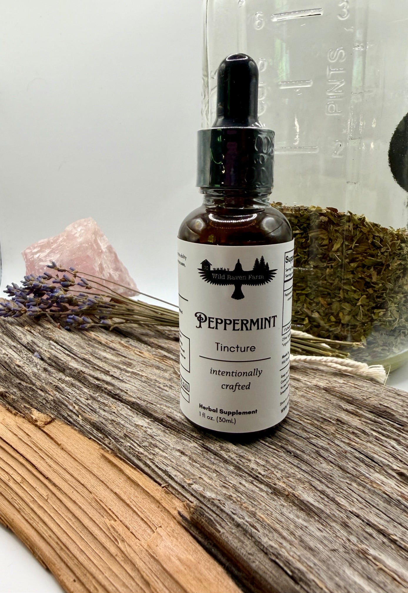 Peppermint tincture bottle on a wooden surface with herbs and a crystal in the background