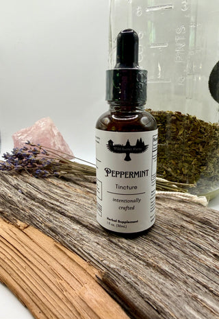 Peppermint tincture bottle on a wooden surface with herbs and a crystal in the background