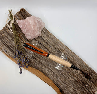 A red, white and black wooden and metal pen displayed on a rustic piece of driftwood with a pink crystal and dried lavender sprigs, against a plain white background. Got to catch them all!
