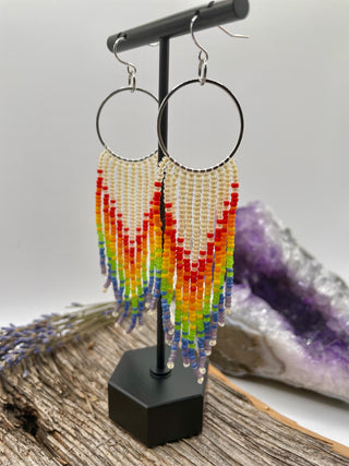 Rainbow beaded earrings on a stand with a natural background