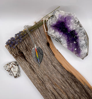 Necklace with a leaf pendant on a wooden surface next to a crystal and dried flowers.