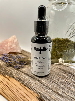 Skullcap tincture bottle on a wooden surface with herbs and a jar in the background