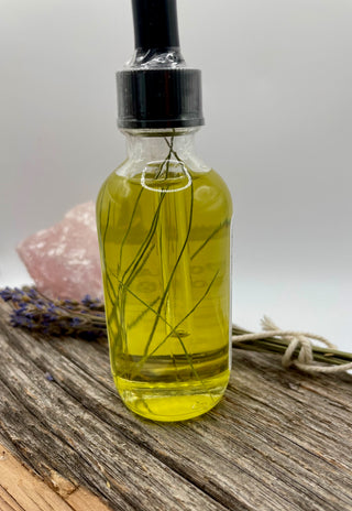 Glass bottle of oil with a dropper and pine needles on a wooden surface with lavender and a crystal.