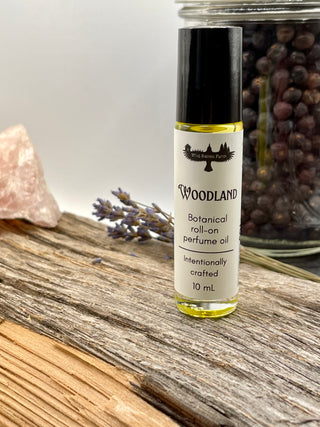 Roll-on perfume oil bottle labeled 'Woodland' on a wooden surface with lavender and rose quartz.