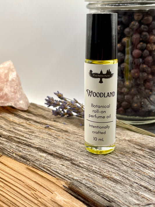Roll-on perfume oil bottle labeled 'Woodland' on a wooden surface with lavender and rose quartz.