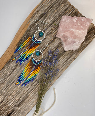 Beaded earrings on a wooden board with a crystal and lavender.