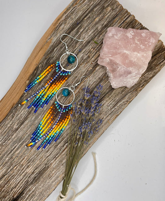 Beaded earrings on a wooden board with a crystal and lavender.